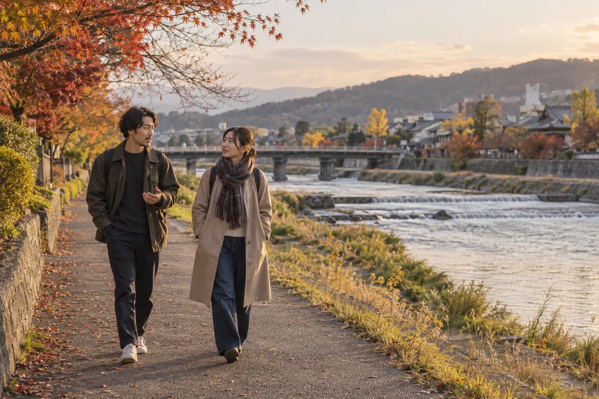 Two friends talking as they walk along a quiet Japanese riverside path in late-afternoon autumn light